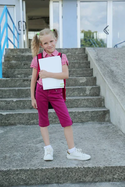 Terug naar school. Mooie blonde schoolmeisje met rode rugzak en boeken buiten de basisschool, onderwijsconcept. — Stockfoto