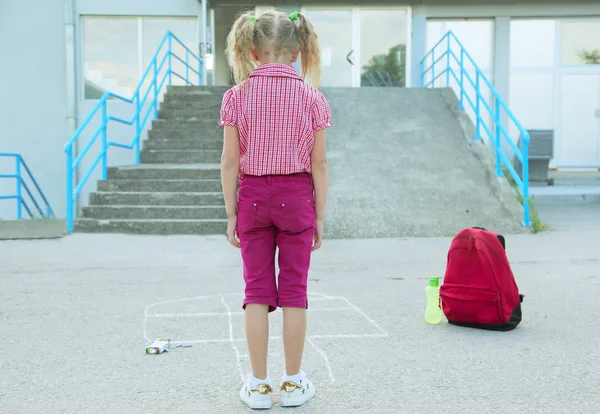 Back to school. Beautiful blond schoolgirl playing hopscotch drawn with colorful chalk on asphalt outside the primary school , education concept. — Stock Photo, Image