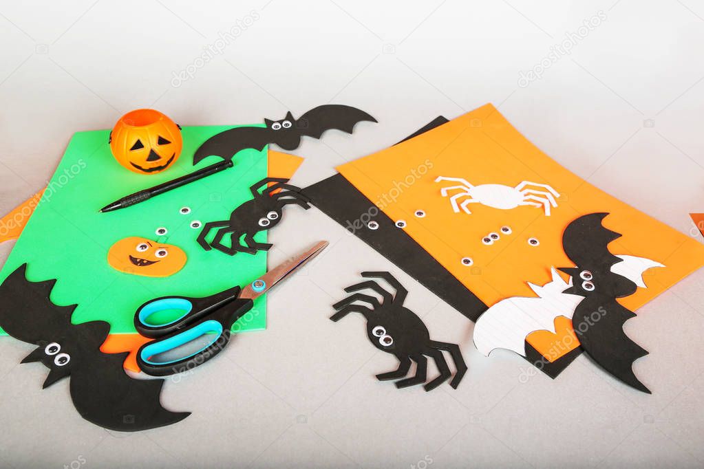 Paper felt Halloween hand made crafts. Felt pumpkin, spider, bat, eyes decorations on gray background. Scissors and materials. 