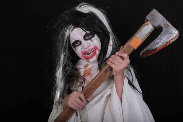 Concepto de horror de Halloween. Linda niña asustadiza en traje de zombi monstruo con hacha de sangre sobre fondo negro . — Foto de Stock