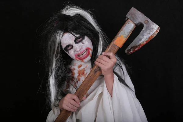 Concepto de horror de Halloween. Linda niña asustadiza en traje de zombi monstruo con hacha de sangre sobre fondo negro . — Foto de Stock