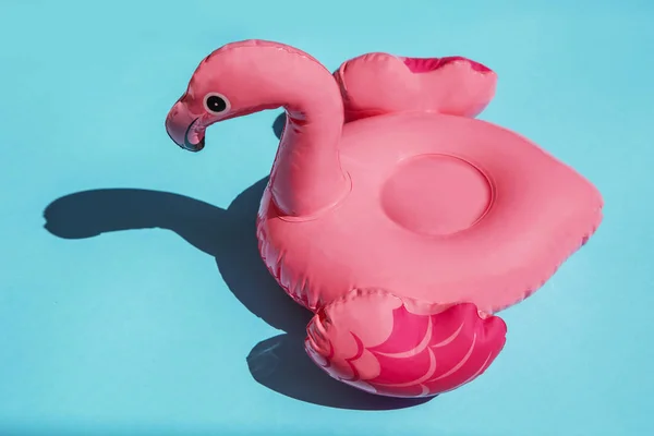 Pink flamingo swim ring drink holder on turquoise background with shadows of exotic plants. — Stock Photo, Image