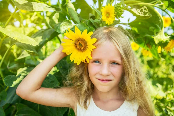 Belle petite fille blonde heureuse sur le champ de tournesol. Fille tient fleur dans la main . — Photo