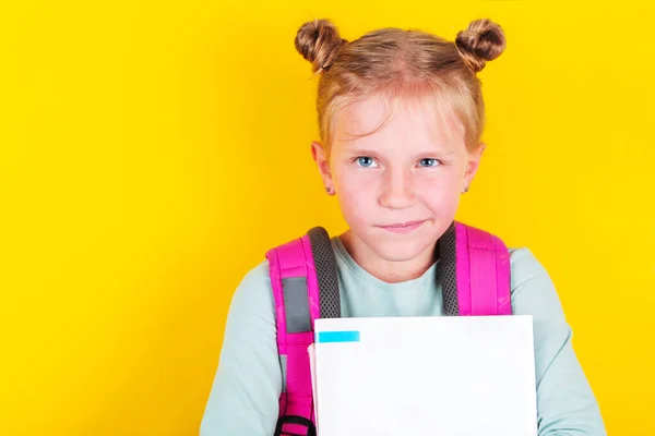 Funny girl from elementary school with book and backpack on yellow background. School concept,education. Back to School. — Stock Photo, Image