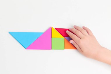 Tangram renkli geometrik yapboz parçaları. Çocuk elleri beyaz masa üzerinde parçaları hareket ettiriyor.. 