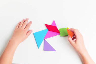 Tangram renkli geometrik yapboz parçaları. Çocuk elleri beyaz masa üzerinde parçaları hareket ettiriyor.. 