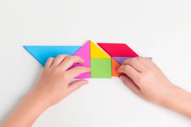 Tangram renkli geometrik yapboz parçaları. Çocuk elleri beyaz masa üzerinde parçaları hareket ettiriyor.. 
