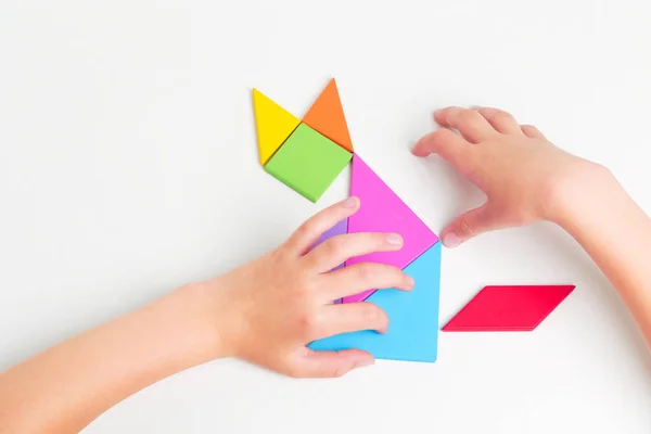 Tangram barevné geometrické puzzle kousky s childs ruce pohybující se kusy na bílém stole, horní pohled. — Stock fotografie