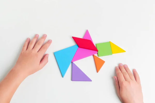 Tangram renkli geometrik yapboz parçaları. Çocuk elleri beyaz masa üzerinde parçaları hareket ettiriyor.. — Stok fotoğraf