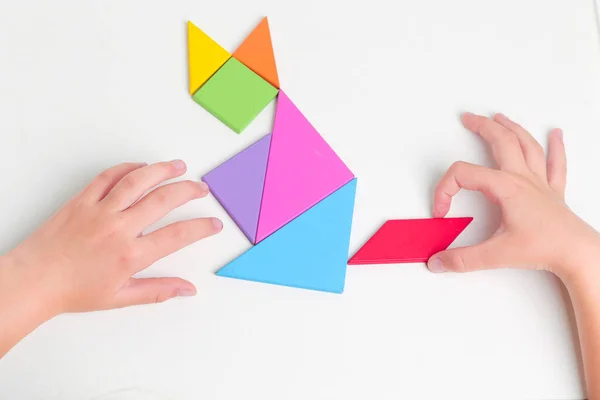Tangram renkli geometrik yapboz parçaları. Çocuk elleri beyaz masa üzerinde parçaları hareket ettiriyor.. 