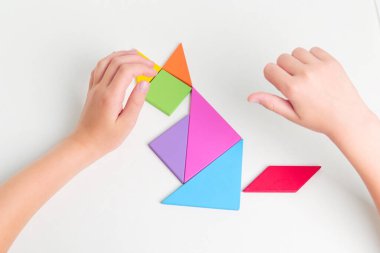 Tangram renkli geometrik yapboz parçaları. Çocuk elleri beyaz masa üzerinde parçaları hareket ettiriyor.. 
