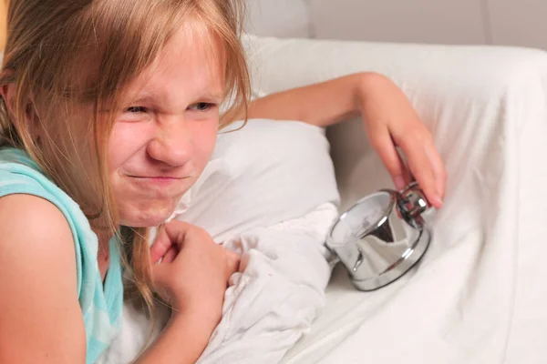 Little funny girl lying in bed and close ears while the alarm clock ring to wake her up in the morning. — Stock Photo, Image