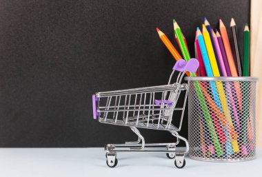 Okul alışveriş konseptine dönelim. Okul malzemeleri ve karatahta arka planında alışveriş arabası. Eğitim, kopyalama alanı.