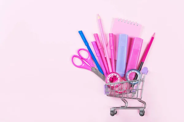 Back to school shopping concept. Colorful school supplies with shopping trolley on pink background. — Stock Photo, Image