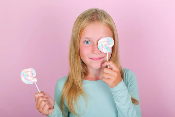 Engraçado sorridente menina cobrir os olhos com pirulitos marshmallow no fundo rosa. — Fotografia de Stock