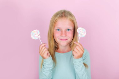 Pembe arka planda lolipopları olan komik, gülümseyen sarışın kız..