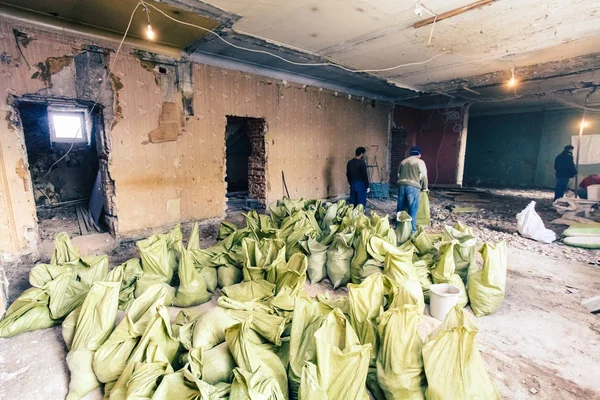 Werknemers klaarmaaltijden bouw vuilnis en afval van de sloop in zakken voor verwijdering in de kamer van het appartement is onder revisie, bouw, verbouwing, wederopbouw en renovatie. — Stockfoto