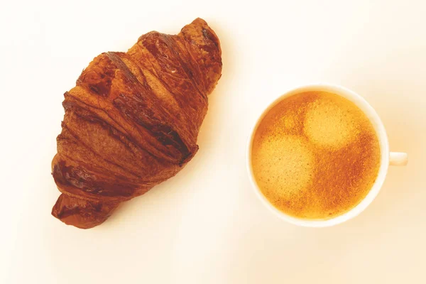 Свежий круассан и чашка кофе - капучино или латте с пенкой на белом фоне с эффектом тонуса . — стоковое фото