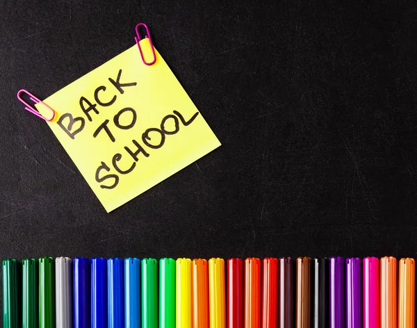 Back to school background with a lot of colorful felt-tip pens and colorful pencils, titles Back to school on the yellow piece of paper or sticker on the black scratched chalkboard — Stock Photo, Image