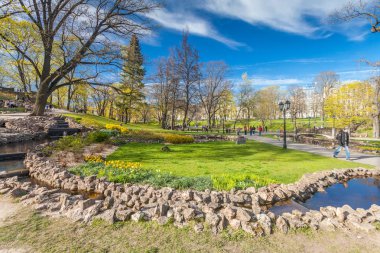 Riga, Letonya - 06 Mayıs 2017: Görünüm çiçeği ağaçlar, çalılar ve Riga şehir merkezi bulunan Park Bastion Hill yürüyen insanlar ile yolları üzerinde. Bastion Hill mo biridir