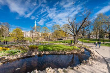 Riga, Letonya - 06 Mayıs 2017: Görünüm çiçeği ağaçlar, çalılar ve Riga şehir merkezi bulunan Park Bastion Hill yürüyen insanlar ile yolları üzerinde. Bastion Hill mo biridir