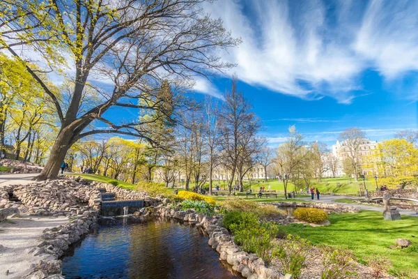 Riga, Letonya - 06 Mayıs 2017: Görünüm çiçeği ağaçlar, çalılar ve Riga şehir merkezi bulunan Park Bastion Hill yürüyen insanlar ile yolları üzerinde. Bastion Hill mo biridir