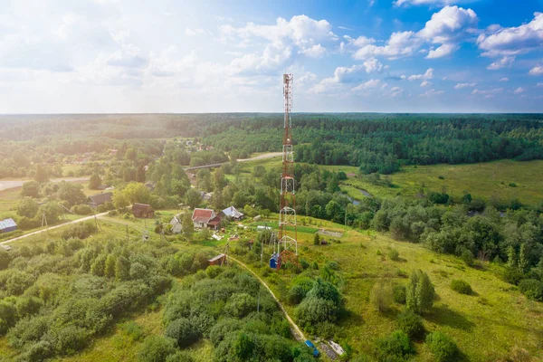 Telecommunication tower with  radio antennas and satellite dishes is installed on the rural on the green field with grass, bushes and trees. Concept of harmless of electromagnetic and microwav