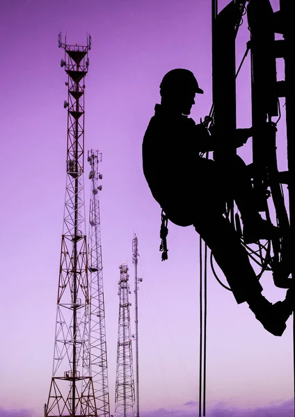 Silhueta de alpinista industrial profissional em capacete e uniforme funciona em altura para a instalação de equipamentos de comunicação e antenas e torres de telecomunicações com céu pôr do sol como fundo. Risco — Fotografia de Stock