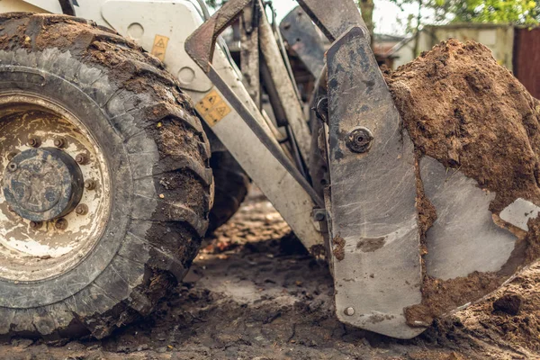 Il moderno escavatore esegue lavori di scavo sul cantiere. Vista sulla grande ruota sporca di terna e sul secchio scavatore che è pieno di terreno di scavo , — Foto Stock