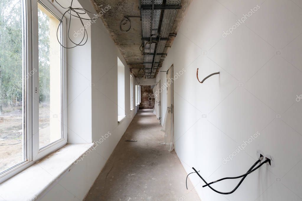 Long and narrow corridor with windows, doors, cable trays and walls with not installed electrical cables in an apartment during on the construction,overhaul, remodeling, rebuilding, home improvements