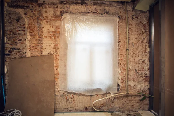 Venster vallende polyethyleen en bakstenen muur met kunststof sanitair pijp in een appartement is onder constructie, revisie, verbouwing, renovatie, restauratie, wederopbouw. — Stockfoto
