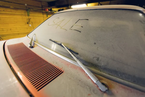 Vista del viejo coche retro americano en garaje con capucha polvorienta pantalla de viento sucio con título VENTA por dedo y limpiaparabrisas roto. Concepto de venta de coches pre-owne . — Foto de Stock