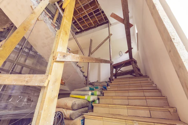 Materiais de construção, fios elétricos, sacos com cimento, claircole e massa de vidraceiro, escadas com corrimão de madeira temporária em um apartamento é durante a construção, remodelação, revisão, reconstrução — Fotografia de Stock