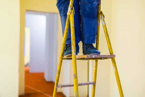 木制梯子上有蓝色工作服和黑色鞋子的工人的腿。工人为公寓石膏墙做石膏板或干墙正在施工、改造、翻新、大修 — 图库照片