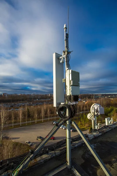 Panel antenna of GSM DCS UMTS LTE bands and radio unit are as part of communication equipment of basic station are installed on the roof and sky and city are as background — Stock Photo, Image