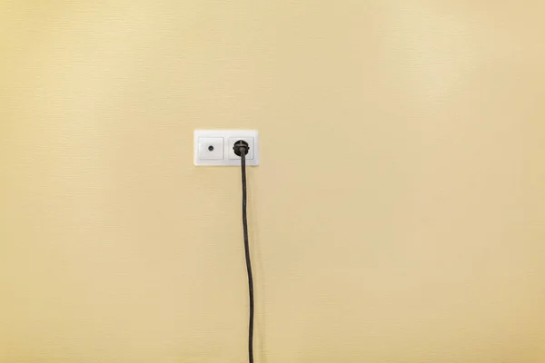 An electrical socket and TV outlet on wall with connected electrical black cable of electrical device in the room in apartment is after construction, remodeling, renovation, overhaul, extension