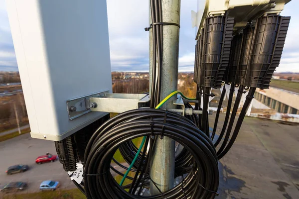 Panel antenna of GSM DCS UMTS LTE bands, GPS antenna and remote radio unit are as part of communication equipment of basic station are installed on the tubular mast and sky and city are as background. — Stock Photo, Image