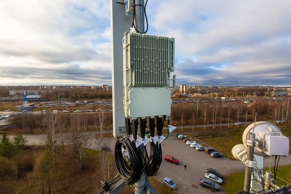 Panel antenna of GSM DCS UMTS LTE bands, GPS antenna and remote radio unit are as part of communication equipment of basic station are installed on the tubular mast and sky and city are as background. — Stock Photo, Image