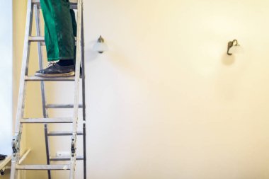 İşçi iş giysisi içinde bir avize yüklüyor ve üzerinde elektrik için bağlanır apartmanda merdiveni tavandan tadilat, yenileme, revizyon, uzantısı, restorasyon yapım aşamasında olan bir