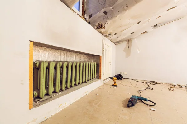 Room with central heating and heating adiator and construction tools on the floor are in apartment that is under construction, remodeling, renovation, overhaul, extension, restoration and