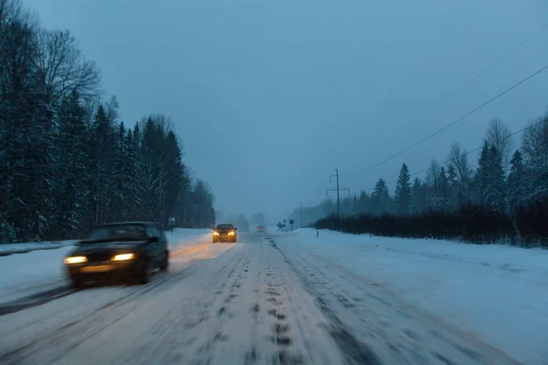 Автомобили ездят с фарами на зимней дороге в снежную бурю в сумерках, когда идет снег. Концепция вождения в опасных условиях с плохой видимостью в зимний период. Изображение: mot — стоковое фото