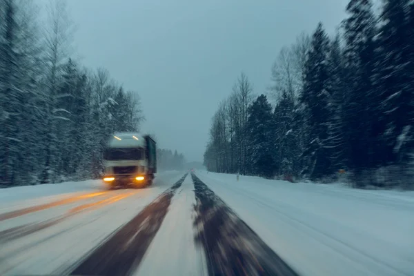 Truck drives with headlights on the winter road in a snow storm in the  twilight  when snow is flying. Concept of driving in the dangerous conditions with bad visibility on the winter. Image with moti