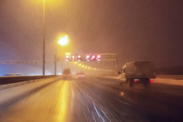 Автомобили быстро ездят по зимнему скоростному шоссе или шоссе с дорожным освещением в снежную бурю в сумерках, когда идет снег с дождём. Концепция вождения в опасных условиях с плохими — стоковое фото