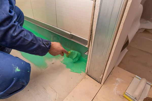 Работник рисует кистью с зеленым цветным водонепроницаемым отделочным материалом пол в ванной комнате в квартире inder строительство, ремонт, ремонт, капитальный ремонт, расширение, реставрация и — стоковое фото