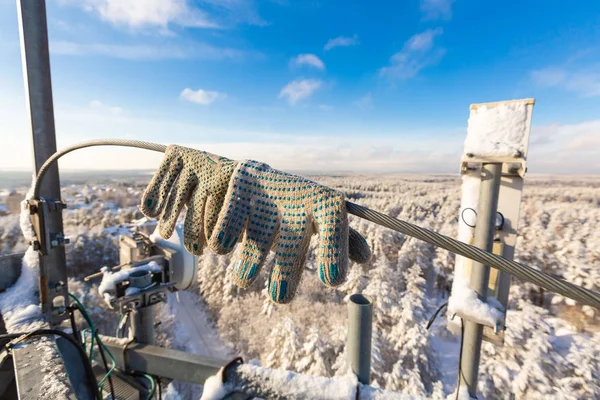 Par de guantes de protección del trabajador-escalador está en la parte superior de la torre de telecomunicaciones con antenas de panel vertical y unidad de radio remota, cables de alimentación y óptica cubiertos por la nieve en el día de invierno . — Foto de Stock