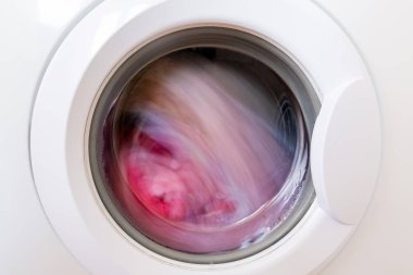 Kapalı yuvarlak çamaşır makinesi kapı içinde dönen giysiler ile. Çerçeve üzerinde kirli çamaşır ve çamaşır makinesinin merkezine odaklanın.