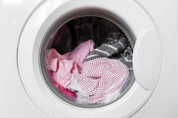 Geschlossene runde Waschmaschinentür mit rotierenden Kleidungsstücken innen. Fokus im Zentrum der schmutzigen Wäsche und Waschmaschine auf dem Rahmen. — Stockfoto