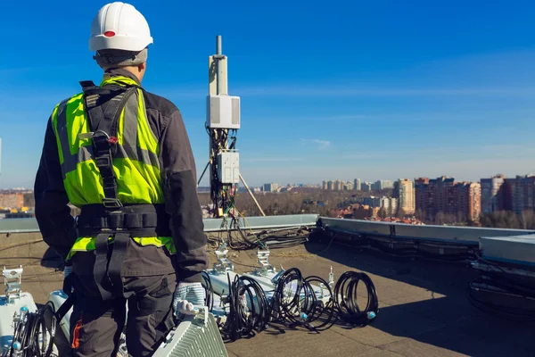 Escalador industrial profesional en casco y uniforme con equipos de telecomunicación en su mano y antenas de bandas GSM DCS UMTS LTE, unidades de radio al aire libre en el techo. Proceso de mejora —  Fotos de Stock