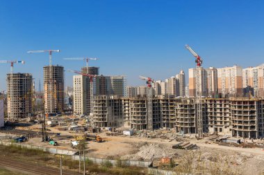 Bir bina kompleksi, işçi, inşaat dişli, araç ve ekipman, kamyon ve arka plan olarak berrak mavi gökyüzü üzerinde çalışan birkaç vinçler de dahil olmak üzere büyük şantiye.