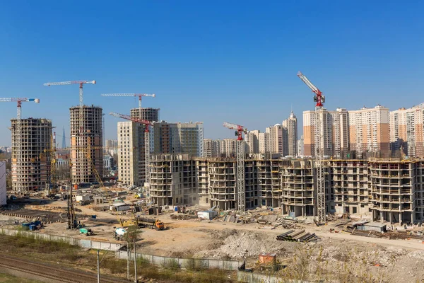 Large construction site including several cranes working on a building complex, workers, construction gear, tools and equipment, trucks and  clear blue sky as background.